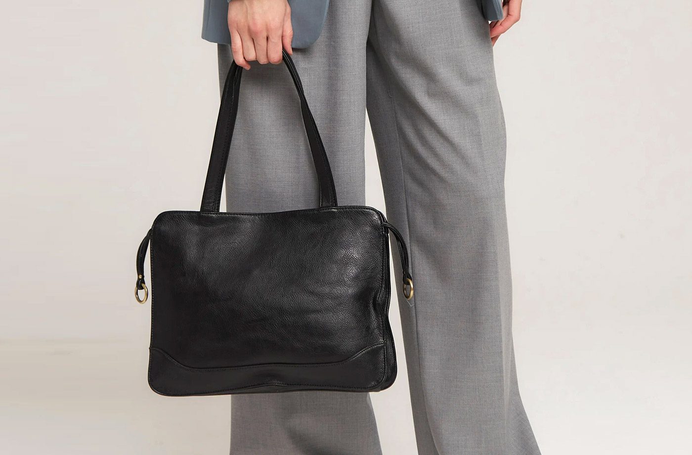 Person holding black leather handbag, wearing suit.