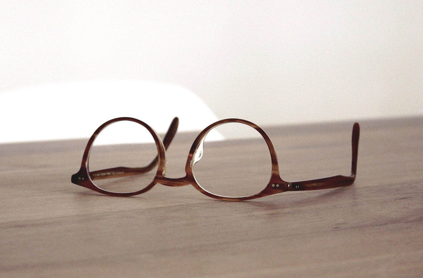 Round eyeglasses on wooden table surface.