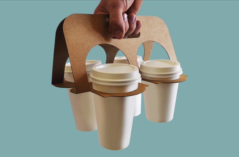 Hand holding cardboard coffee cup carrier.