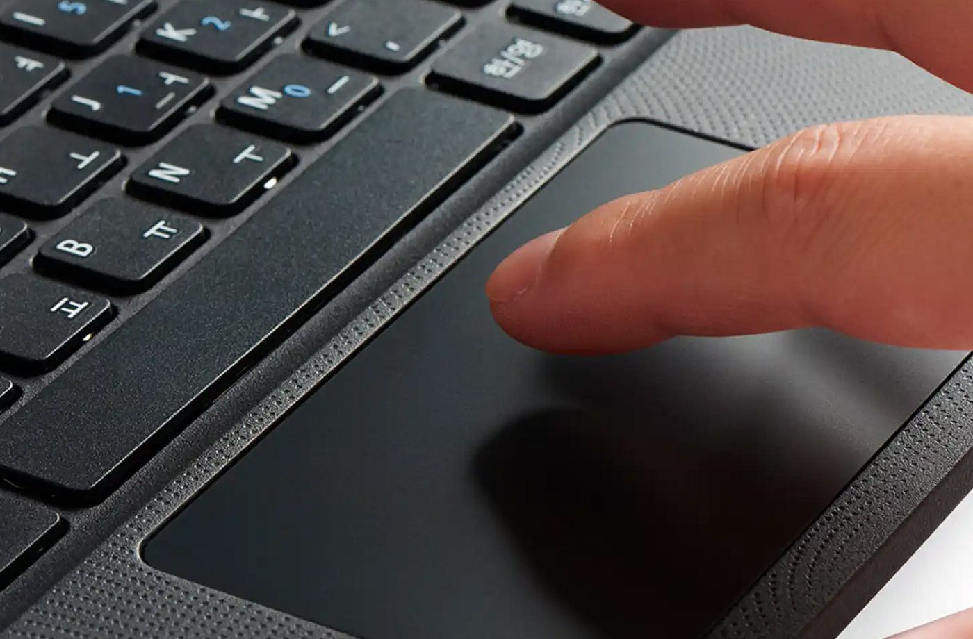 Finger touching laptop trackpad near keyboard.