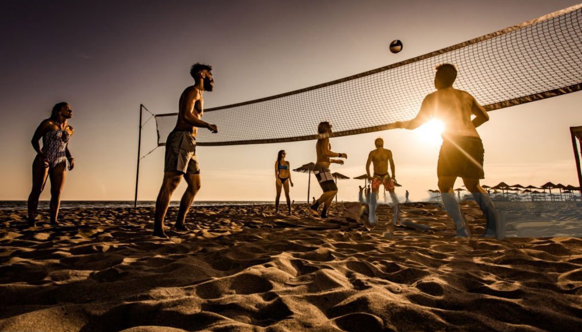 People playing beach volleyball at sunset.